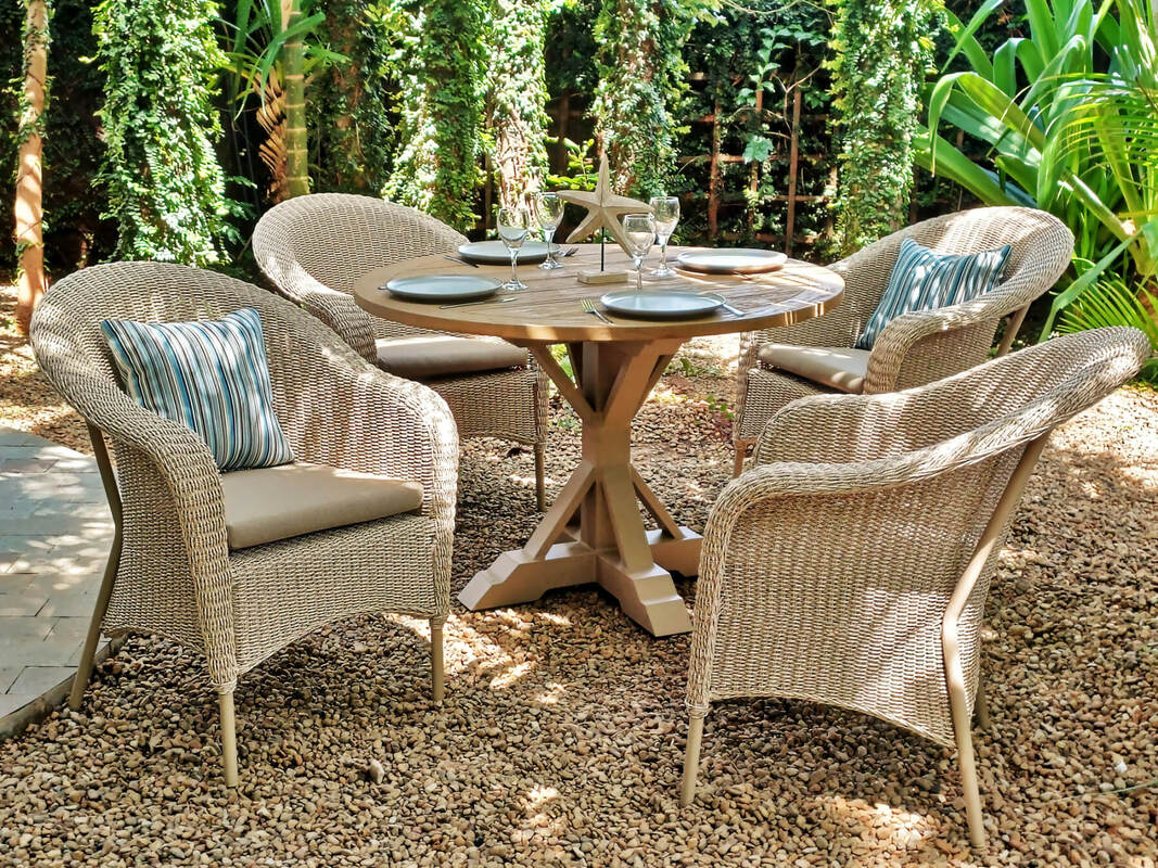 Conjunto de comedor de exterior con mesa de madera de teca y sillones trenzados en un jardin tropical con suelo de guijarros de piedra en una villa en Marbella, Málaga, Costa del Sol