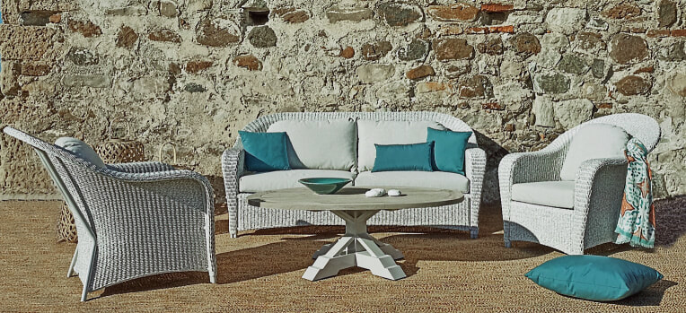 Conjunto de un sofá y dos sillones de trenzado de  color gris con mesa de teca y cojines azules en una casa rústica en Estepona